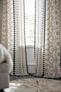 Detail view of black geometric pattern on cotton linen curtains with black tassel fringe