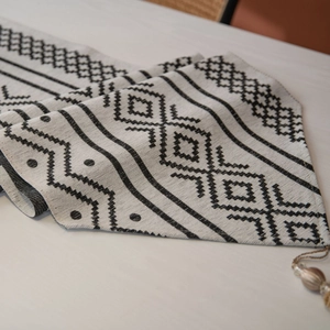 Chemin de table en jacquard moderne avec motifs géométriques noirs et glands sur bois