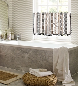 Rideau géométrique bohème avec bordure à pompons noirs dans une salle de bain lumineuse