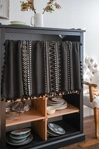 Detail of bohemian geometric black cabinet curtain with elegant fringe and tassels