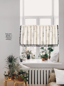 Detail of beige cafe curtain featuring black floral prints and decorative pom pom tassels
