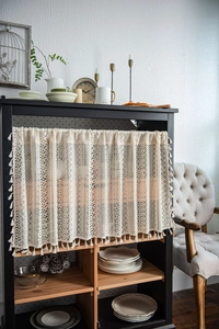 Detailed macro view of crochet floral lace curtain with fringe tassels on a cabinet