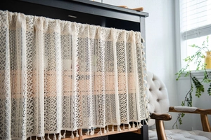 Detail of cream lace short curtain with geometric hollow patterns and fringe tassels