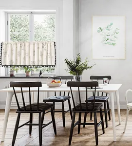 Close-up of beige linen floral cafe curtain with black pom-pom fringe in a bright kitchen