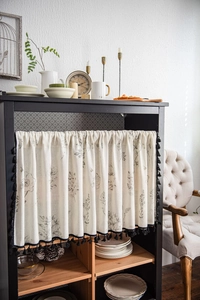 Detail of floral print cabinet curtain with elegant black tassel trim for home decor