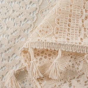Detailed macro view of cream crochet lace fabric with intricate patterns and tassel fringe