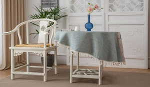 Detail of light blue jacquard tablecloth with elegant cream fringe on a small table