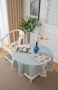 Detail of round light blue tablecloth featuring geometric embroidery and white tassel fringe
