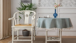 Detail of light blue jacquard tablecloth with creamy tassels on a round dining table