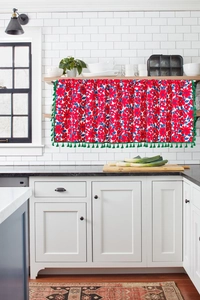 Detail of red floral kitchen half curtain with green fringe trim on white backdrop