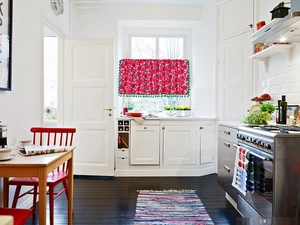 Macro detail of red floral kitchen cafe curtain with green fringe tassels on a white base