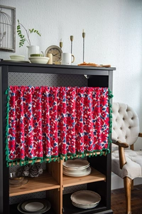 Close-up of rustic floral cabinet curtain with dense green fringe tassels on black shelf