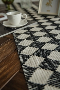 Detailed view of woven black and white diamond pattern table runner on a wooden surface