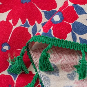 Detail of red floral print fabric with green tassels and linen texture for cabinet curtain