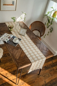 Detail of diamond weave table runner with cotton fringes on a rustic wood surface