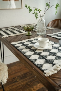 Close-up of black and white diamond pattern woven placemats with tassel edges on a table