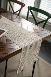 Detail of hand-woven hollow-out table runner with fringe on vintage wood table