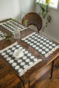 Close-up of woven placemat featuring black and white diamond patterns with fringe tassels