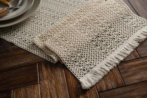 Detail of hand-woven beige table runner with hollow geometric patterns and fringe