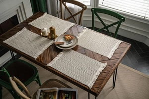 Close-up of bohemian woven placemats with cream tassels on a rustic dark wooden dining table