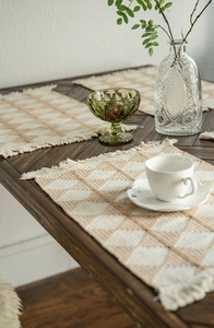 Close-up of woven cotton table runner with beige diamond patterns and handmade tassels
