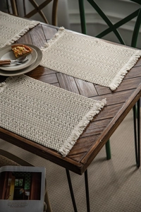 Close-up of handmade macrame table placemats with fringe details on a dark wood table