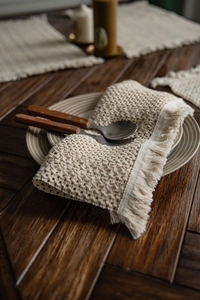 Detail of woven table mat with fringe tassels on dark wood table with ceramic plate