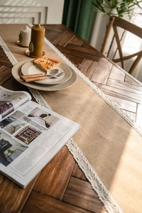 Detail of natural jute table runner with delicate white lace edge on dark wood table