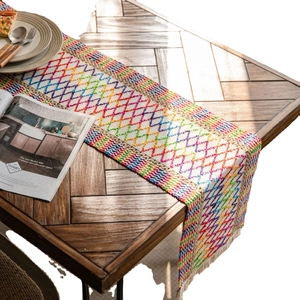 Rainbow woven table runner with diamond hollow pattern and white tassels on wooden table