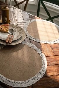 Detail of round natural jute placemat with white wavy lace edges on wooden table