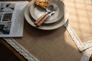 Detail of natural burlap table runner with white crochet lace edges on wooden table