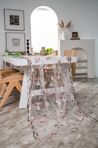 Detail of pink floral embroidery on white lace table runner with natural draping