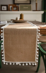 Macro view of woven natural jute table runner with white decorative pom-pom fringe