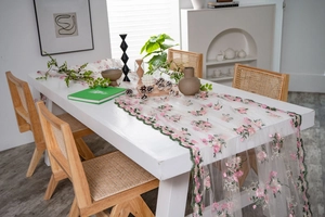 Close-up of pink flower embroidery and green scalloped edges on lace table runner