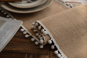 Detailed close-up of natural jute table runner with white pom-pom trim on wood table