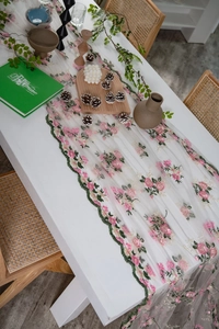 Close-up of floral embroidery with pink roses and green leaves on a mesh tablecloth
