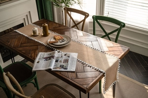 Macro detail of natural burlap table runner with white pom-pom fringe on a wooden table