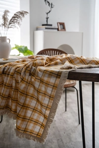 Detail of yellow and white plaid tablecloth with delicate cream tassels on a wooden table