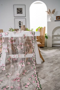 Close-up of pink flower embroidery on white mesh table runner with green wavy edges