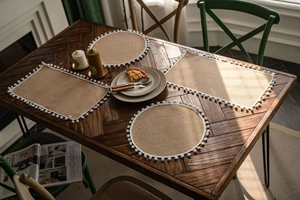 Close-up of natural jute table mat set featuring elegant white pom-pom lace trim