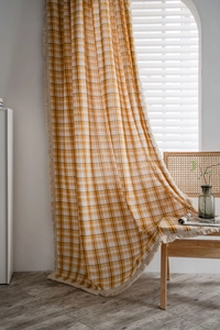 Close-up of yellow plaid curtain fabric with cream tassel fringe in natural light