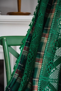 Detail of green plaid fabric curtain featuring delicate crochet lace trim and tassels