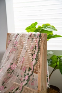 Detail showing pink flower embroidery on lace fabric draped over a vintage wooden chair