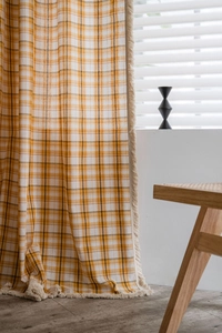 Detail of plaid curtains with cream tassels in warm yellow and brown cotton-linen fabric