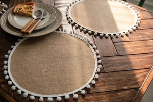 Detailed close-up of woven natural jute placemat with white decorative pom-pom fringe