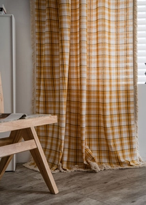 Detail view of yellow plaid curtain with white tassels and a natural linen texture