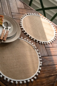 Detail of round natural jute placemats with white pom-pom trim on a dark wooden table