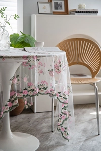 Close-up of white lace tablecloth with pink flower embroidery and scalloped edges