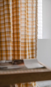 Detailed view of yellow and black plaid curtain fabric with decorative fringe tassels