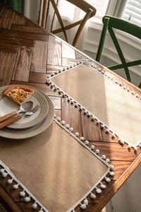 Detail of natural jute table runner with white pom-poms on a dark wood grain table